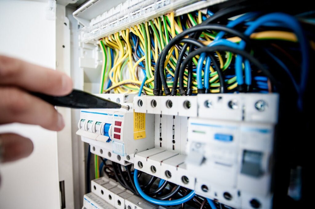 Hand of electrician working on a circuit breaker panel with colorful wires, ensuring safe electrical connections.